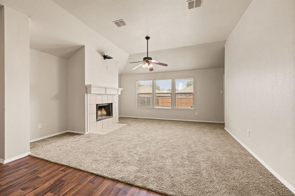 5509 Timber Ridge Court Watauga, TX 76137 - Photo 17 of 28 Vaulted ceiling with an integrated ceiling fan, a tiled fireplace featuring a mantel, multiple windows, and a carpeted floor