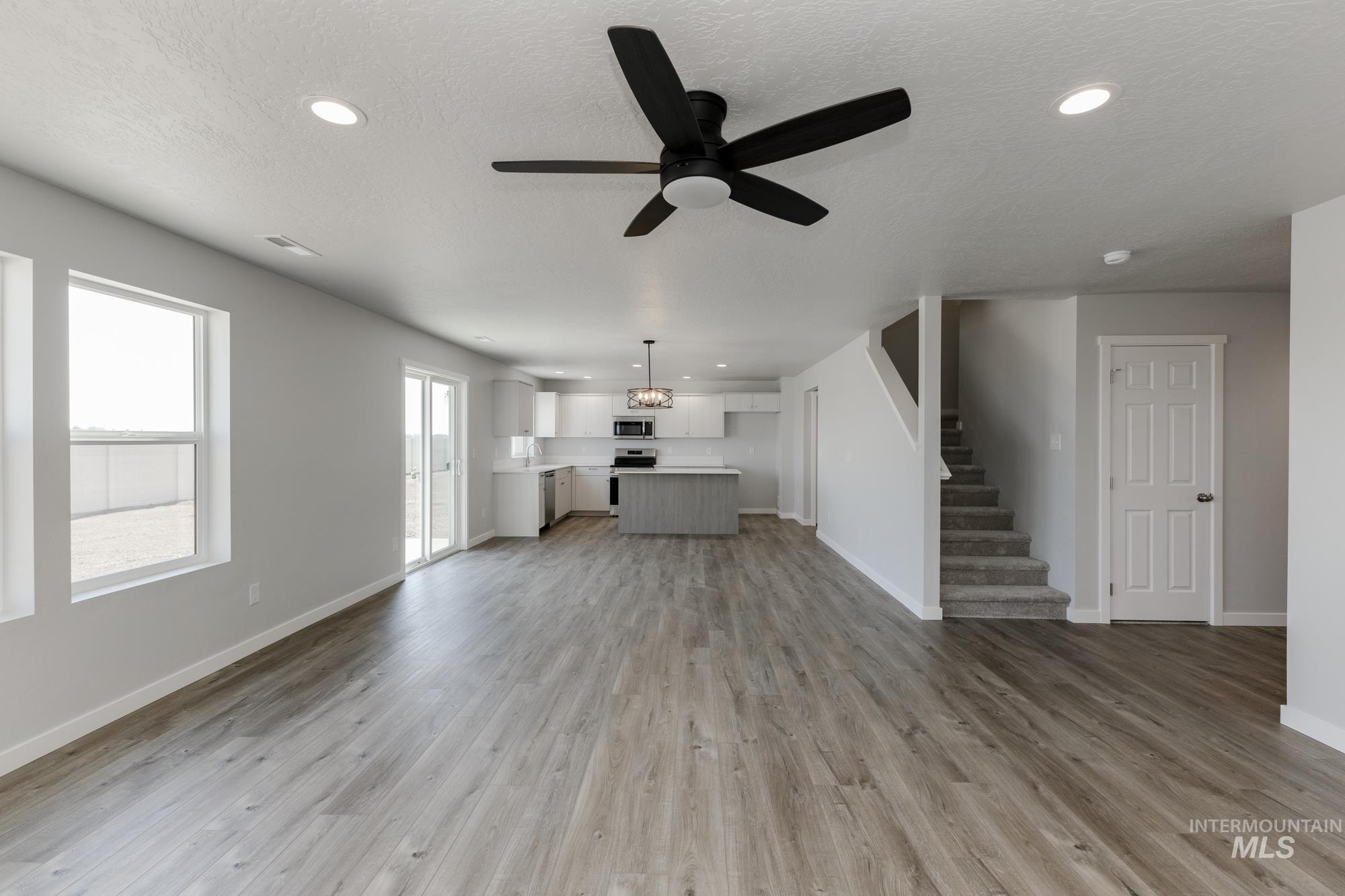 16366 Backfill Avenue Caldwell, ID 83607 - Photo 10 of 24 Unfurnished living room with a textured ceiling, a ceiling fan, light wood finished floors, stairs, and recessed lighting