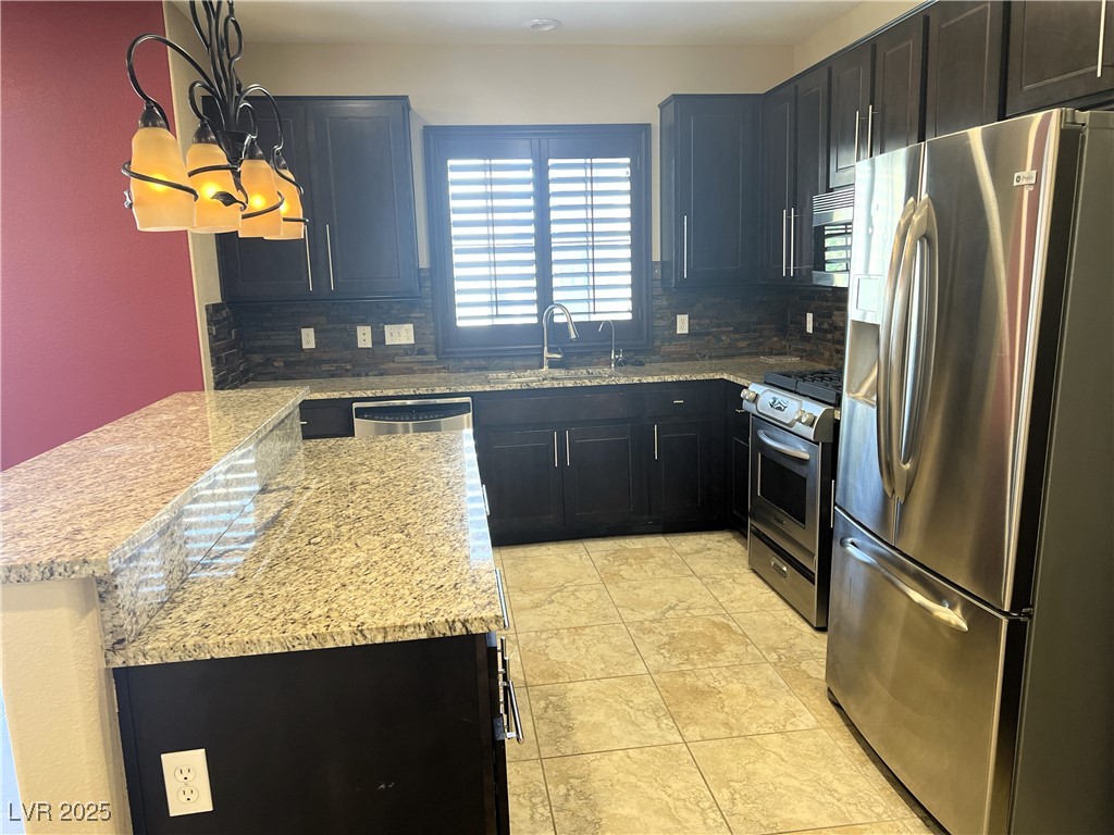 9535 Leaping Lizard Street Las Vegas, NV 89178 - Photo 4 of 37 Kitchen with a sink, appliances with stainless steel finishes, a peninsula, light stone countertops, and backsplash