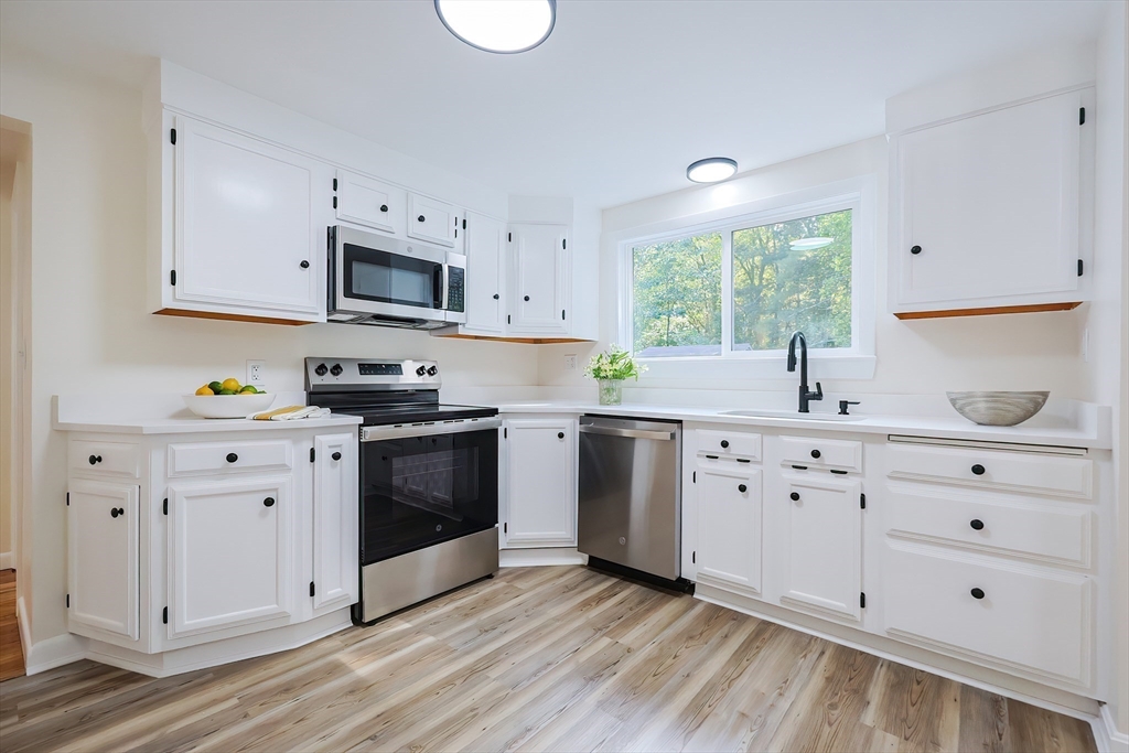 16 Deerfield Road Sharon, MA 02067 - Photo 4 of 38 a kitchen with granite countertop white cabinets a white stove a sink and dishwasher with wooden floor