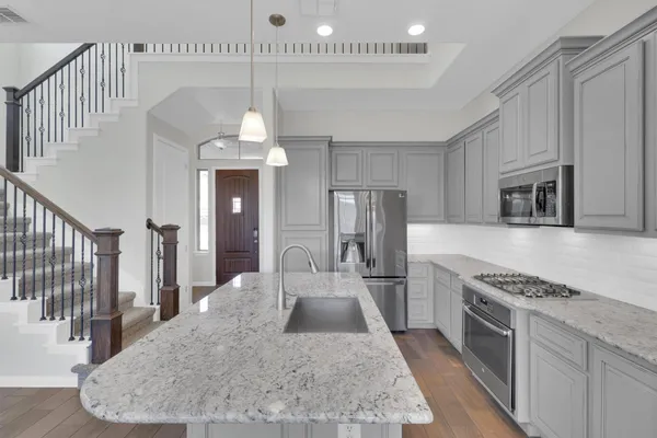 a kitchen with stainless steel appliances kitchen island granite countertop a stove a sink dishwasher and a refrigerator with wooden floor