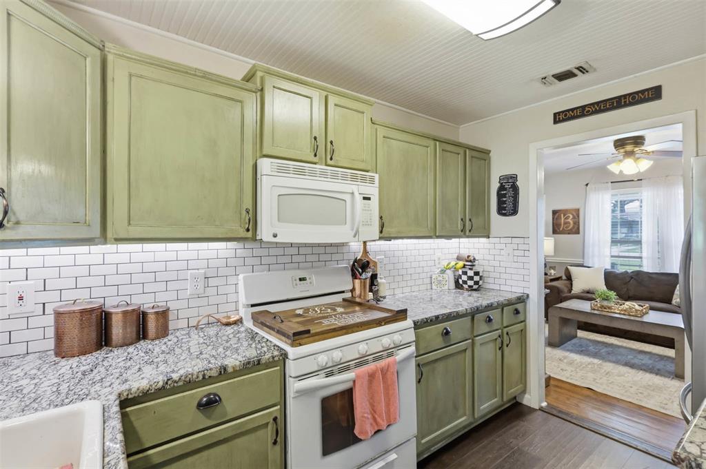 308 West 1st Street Springtown, TX 76082 - Photo 14 of 39 Kitchen featuring green cabinetry, granite-style countertops, white subway tile backsplash, and a built-in microwave