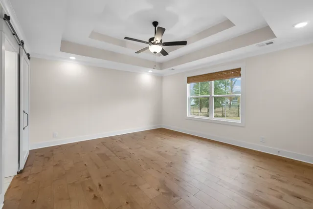 an empty room with wooden floor ceiling fan and windows