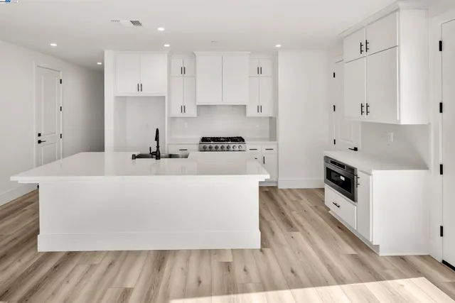 a white kitchen with wooden floor and stainless steel appliances