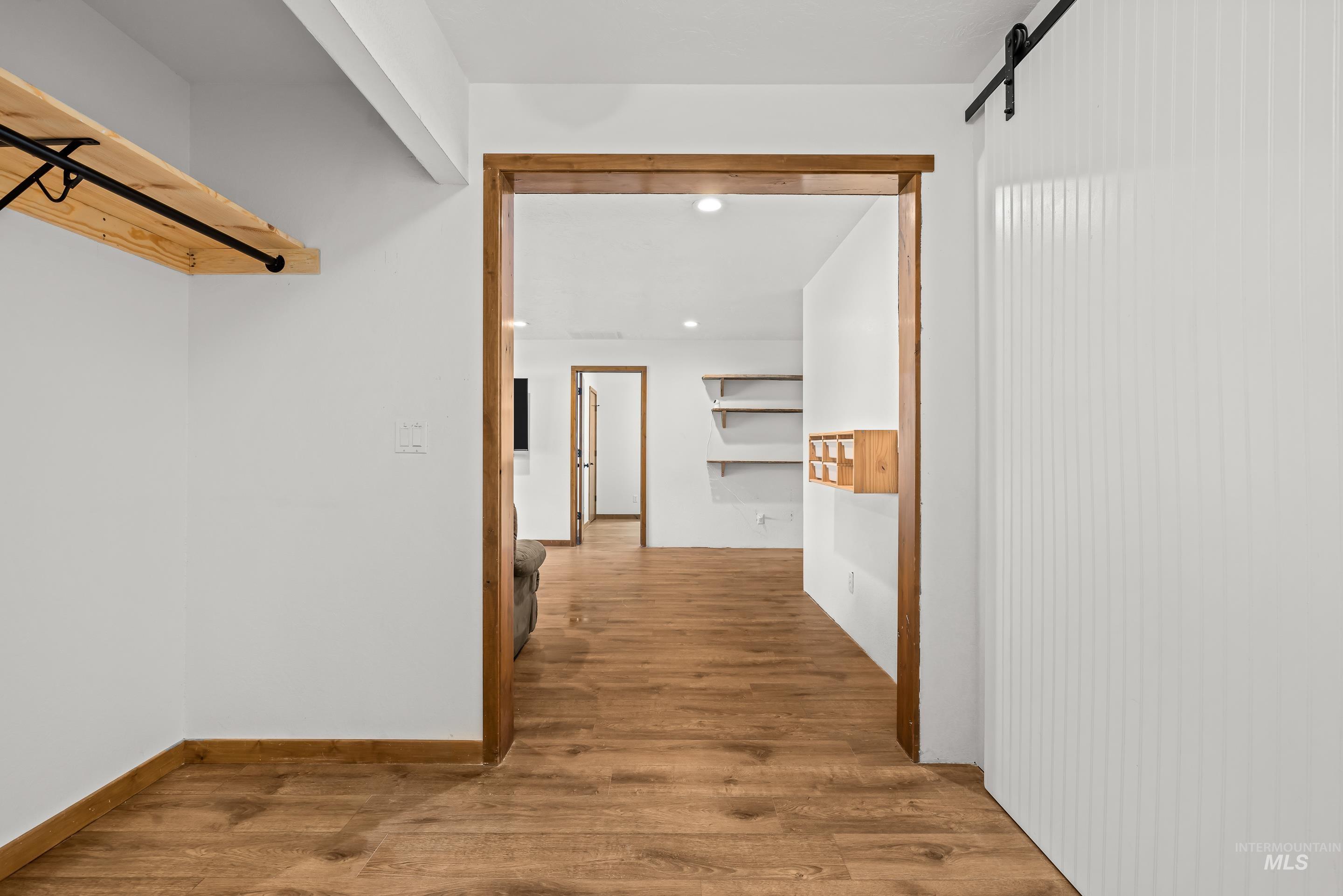 92 Cruickshank Road Horseshoe Bend, ID 83629 - Photo 29 of 50 Interior hallway featuring wood-finish flooring, a white paneled barn door, and a built-in wood-shelf storage system