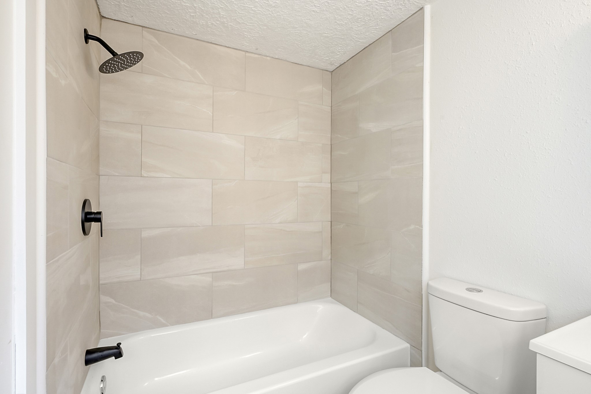 29615 Brookchase Drive Spring, TX 77386 - Photo 18 of 24 This bathroom features a modern design with neutral large tiles, a sleek black showerhead, and a matching faucet. It includes a bathtub and a compact toilet, creating a clean and look.