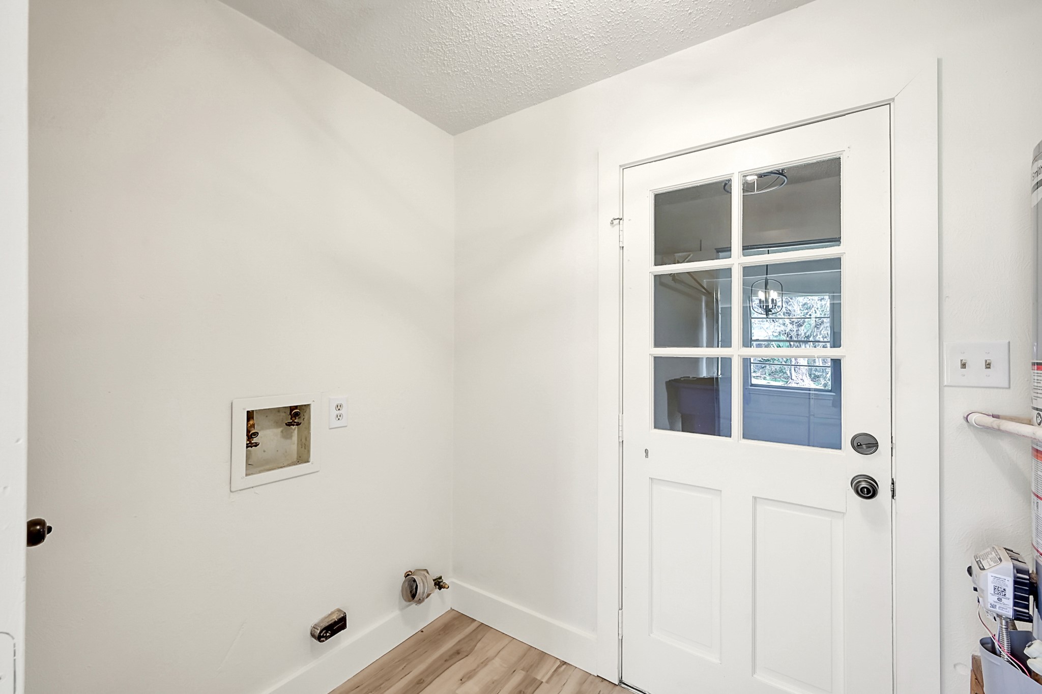 29615 Brookchase Drive Spring, TX 77386 - Photo 22 of 24 This is a small utility room with a washer/dryer hookup, featuring a white door with glass panels, neutral walls, and light vinyl plank wood flooring.