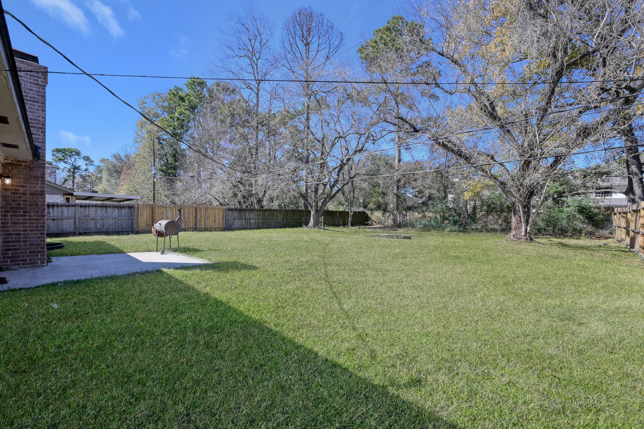 29615 Brookchase Drive Spring, TX 77386 - Photo 23 of 24 Spacious backyard with a well-maintained lawn, mature trees, a wooden fence for privacy, and a small patio area with a grill, perfect for outdoor activities.