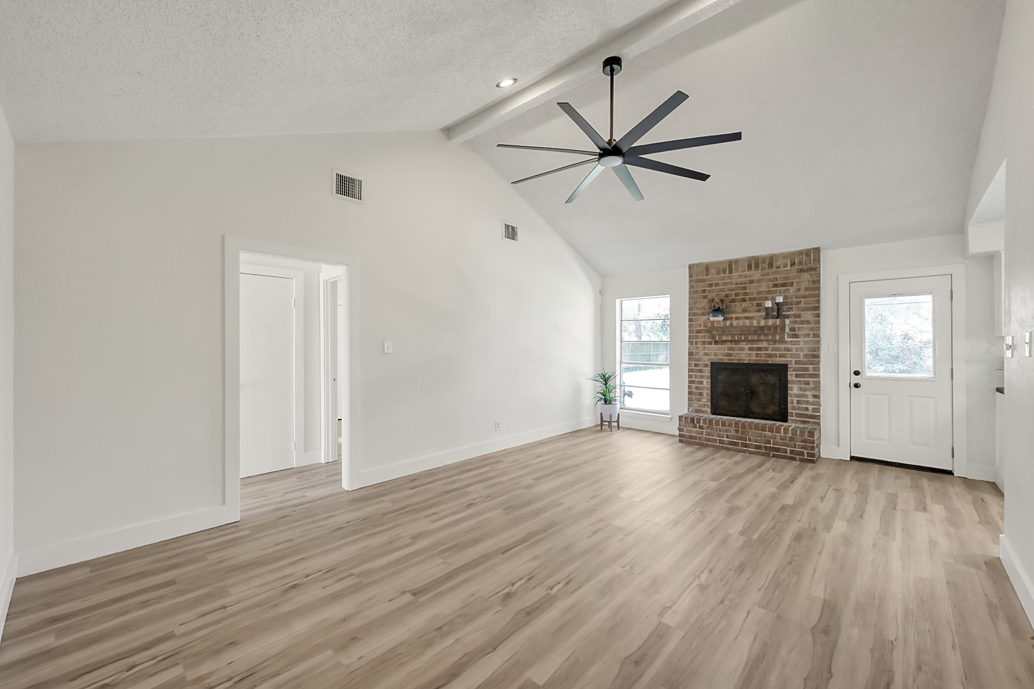 29615 Brookchase Drive Spring, TX 77386 - Photo 5 of 24 This spacious living room features light wood style flooring, a vaulted ceiling with a modern fan, and a cozy brick fireplace. Natural light streams through large windows, creating a bright and inviting atmosphere.