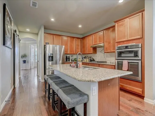 a kitchen with stainless steel appliances granite countertop a refrigerator a stove and a sink with wooden floor