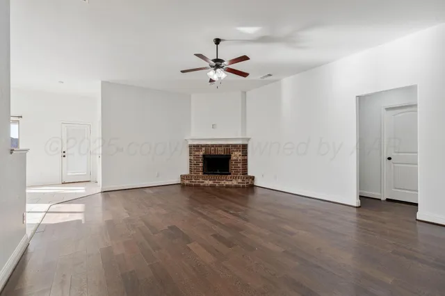 an empty room with wooden floor a ceiling fan a fireplace and a window