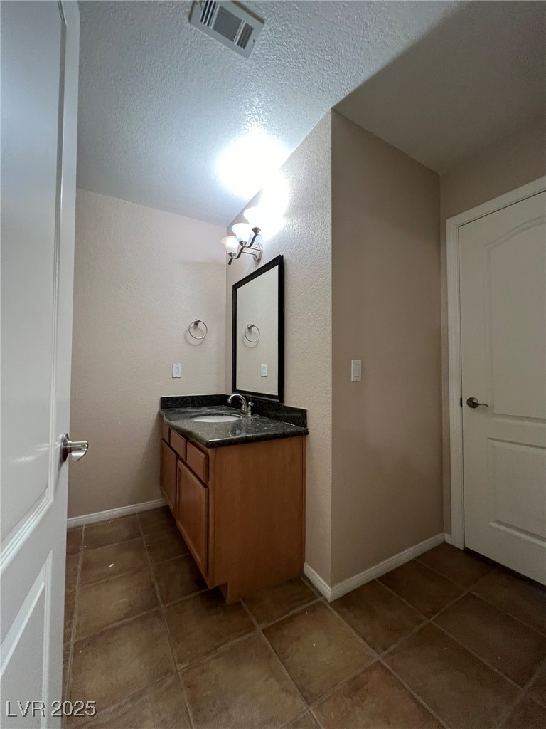 9325 West Desert Inn Road, Unit 206 Las Vegas, NV 89117 - Photo 18 of 37 Bathroom with vanity, a textured ceiling, dark tile patterned floors, and a textured wall