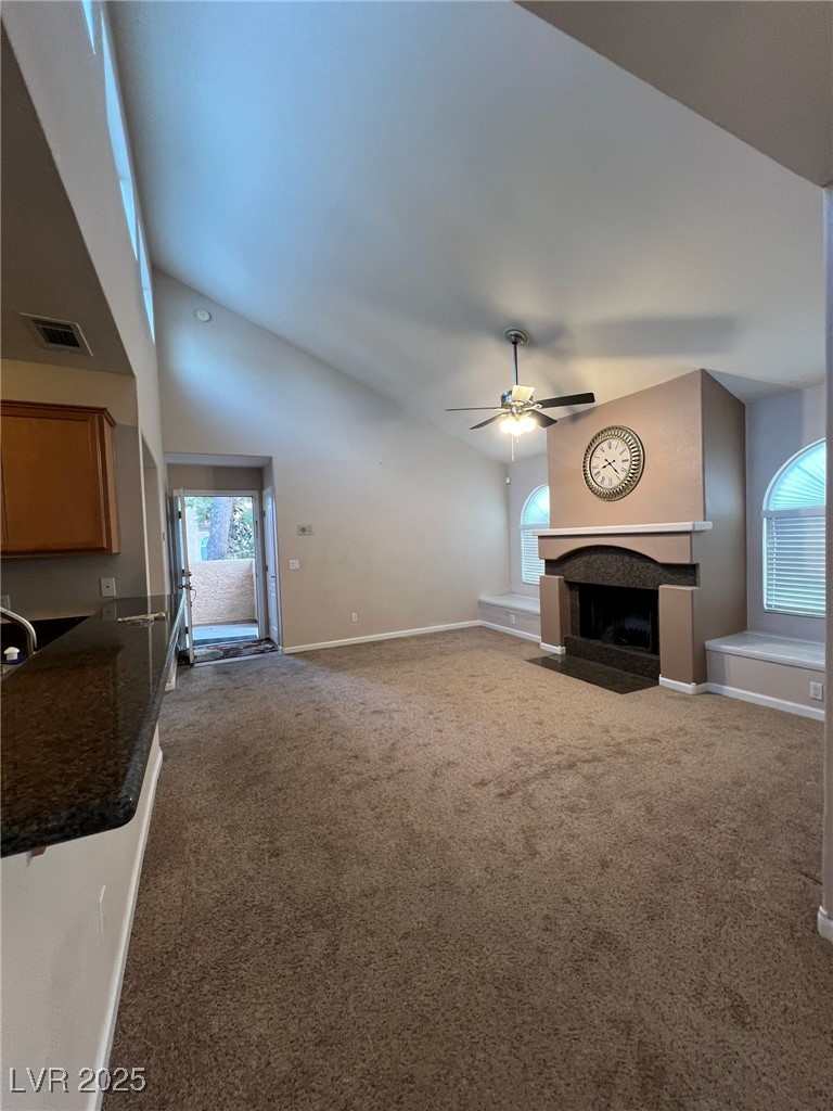 9325 West Desert Inn Road, Unit 206 Las Vegas, NV 89117 - Photo 31 of 37 Unfurnished living room featuring a fireplace with flush hearth, plenty of natural light, carpet flooring, high vaulted ceiling, and ceiling fan