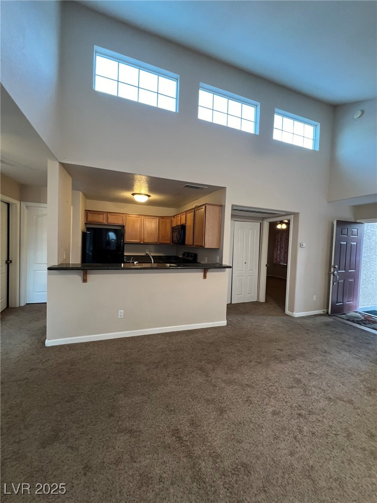 9325 West Desert Inn Road, Unit 206 Las Vegas, NV 89117 - Photo 36 of 37 Kitchen with a high ceiling, dark countertops, brown cabinetry, dark colored carpet, and open floor plan