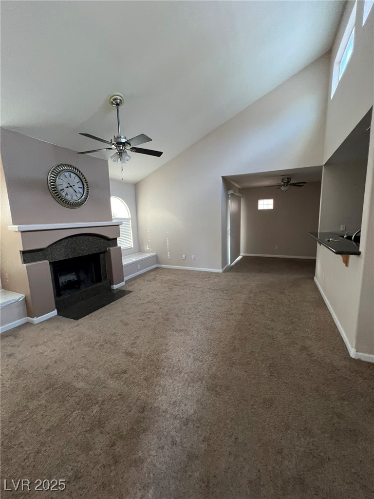 9325 West Desert Inn Road, Unit 206 Las Vegas, NV 89117 - Photo 3 of 37 Unfurnished living room featuring ceiling fan, a fireplace with flush hearth, carpet, and high vaulted ceiling