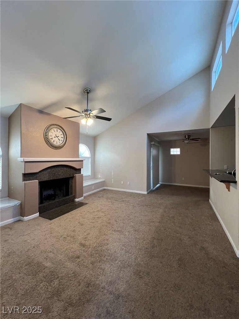9325 West Desert Inn Road, Unit 206 Las Vegas, NV 89117 - Photo 7 of 37 Unfurnished living room featuring ceiling fan, healthy amount of natural light, a fireplace, carpet flooring, and high vaulted ceiling
