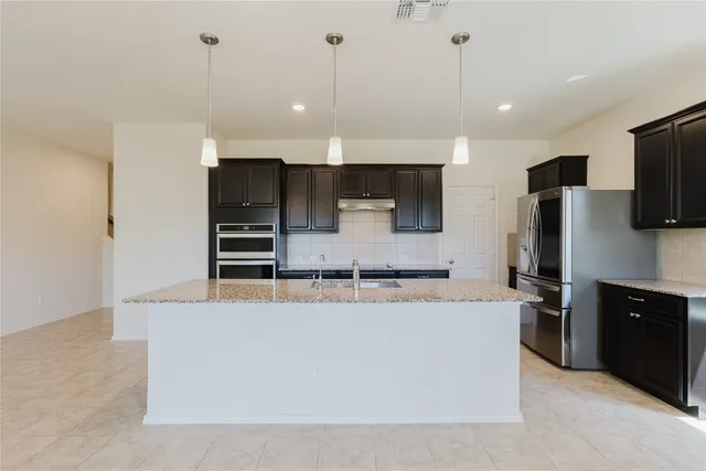 a large kitchen with kitchen island a large counter top stainless steel appliances and cabinets