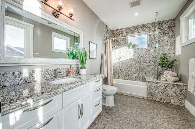 a bathroom with a granite countertop sink mirror vanity bathtub and a toilet