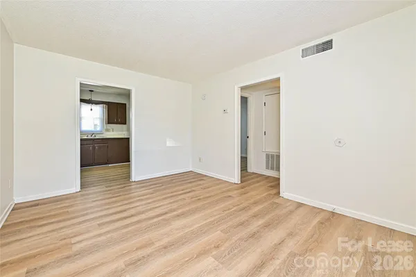 a view of an empty room with wooden floor & kitchen view