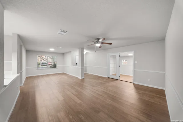 an empty room with wooden floor chandelier fan and windows