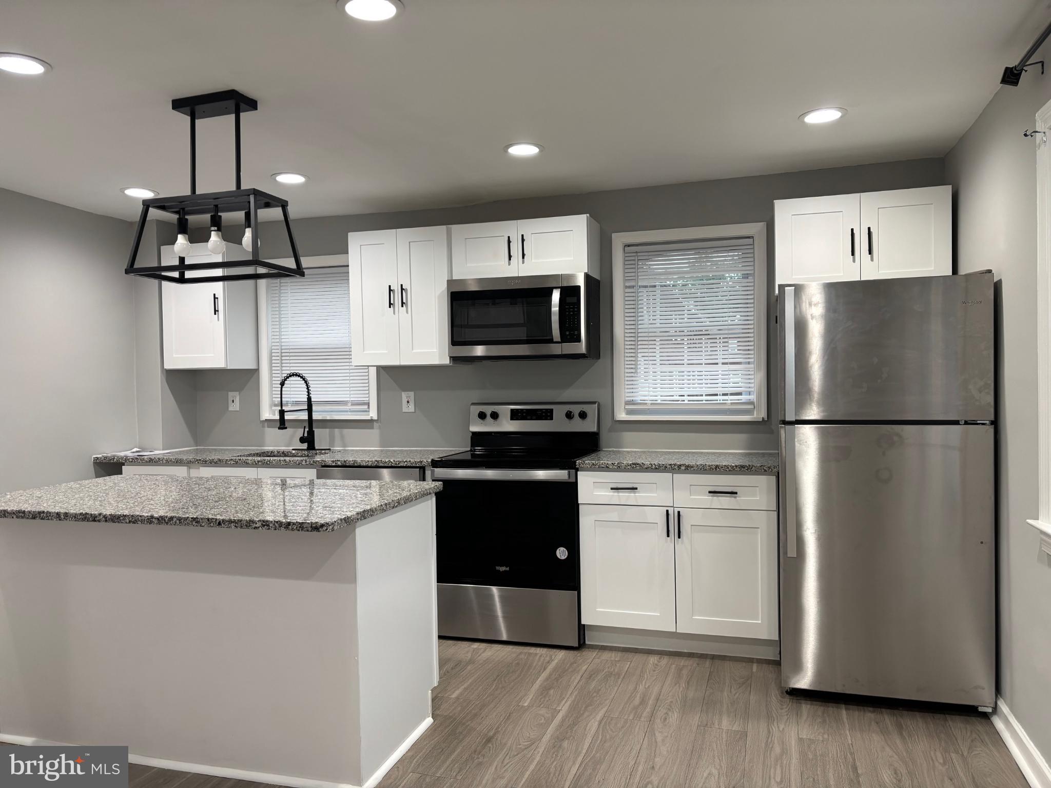 a kitchen with stainless steel appliances granite countertop a refrigerator a stove a sink a microwave and wooden floor