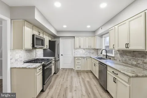 a kitchen with stainless steel appliances granite countertop a stove top oven a sink dishwasher a refrigerator and white cabinets with wooden floor