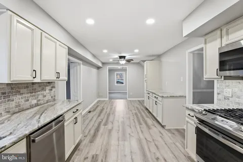 a kitchen with granite countertop a stove top oven a sink dishwasher a refrigerator and white cabinets with wooden floor