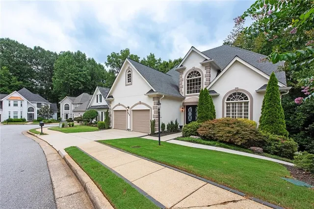 a view of a yard in front of a house with plants and large trees