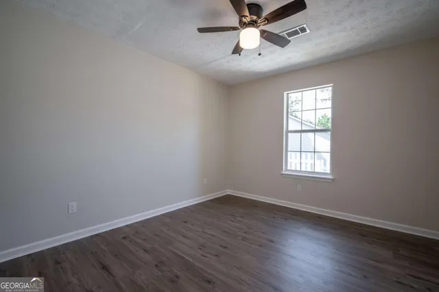 an empty room with wooden floor fan and windows
