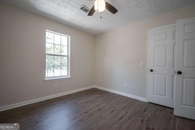 an empty room with wooden floor chandelier fan and windows