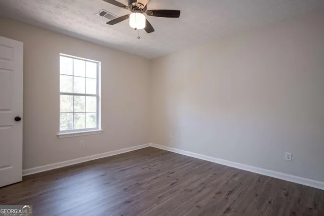 an empty room with wooden floor fan and windows