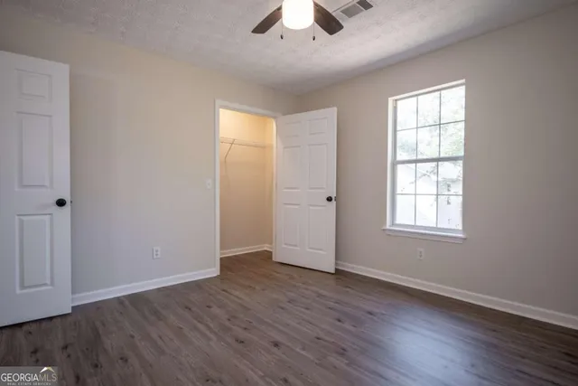 an empty room with wooden floor chandelier fan and windows