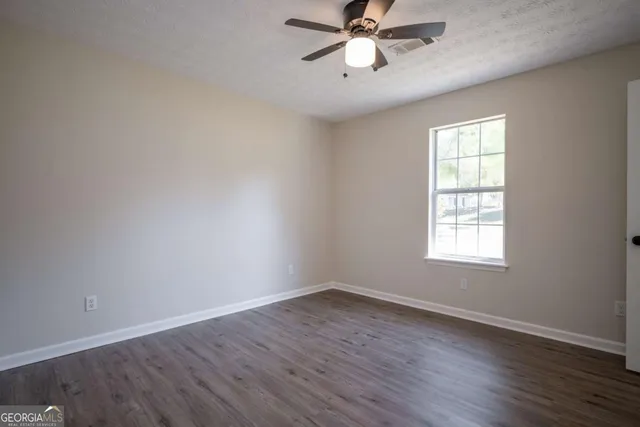 an empty room with wooden floor fan and windows