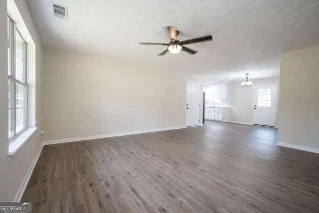 an empty room with wooden floor fan and windows