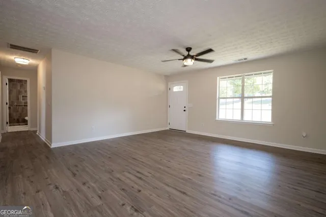 an empty room with wooden floor chandelier fan and windows