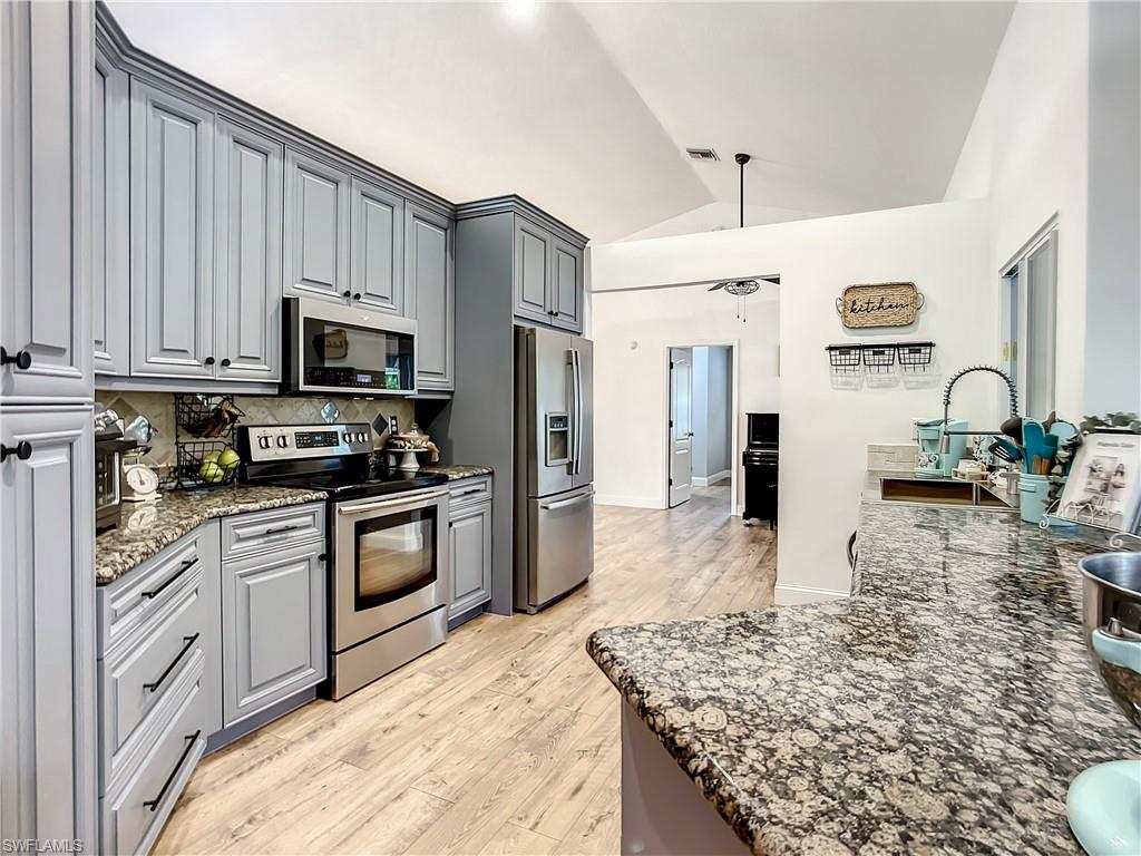 10231 Boca Circle Naples, FL 34109 - Photo 15 of 44 a kitchen with stainless steel appliances granite countertop a stove top oven a sink a refrigerator with white cabinets and wooden floor