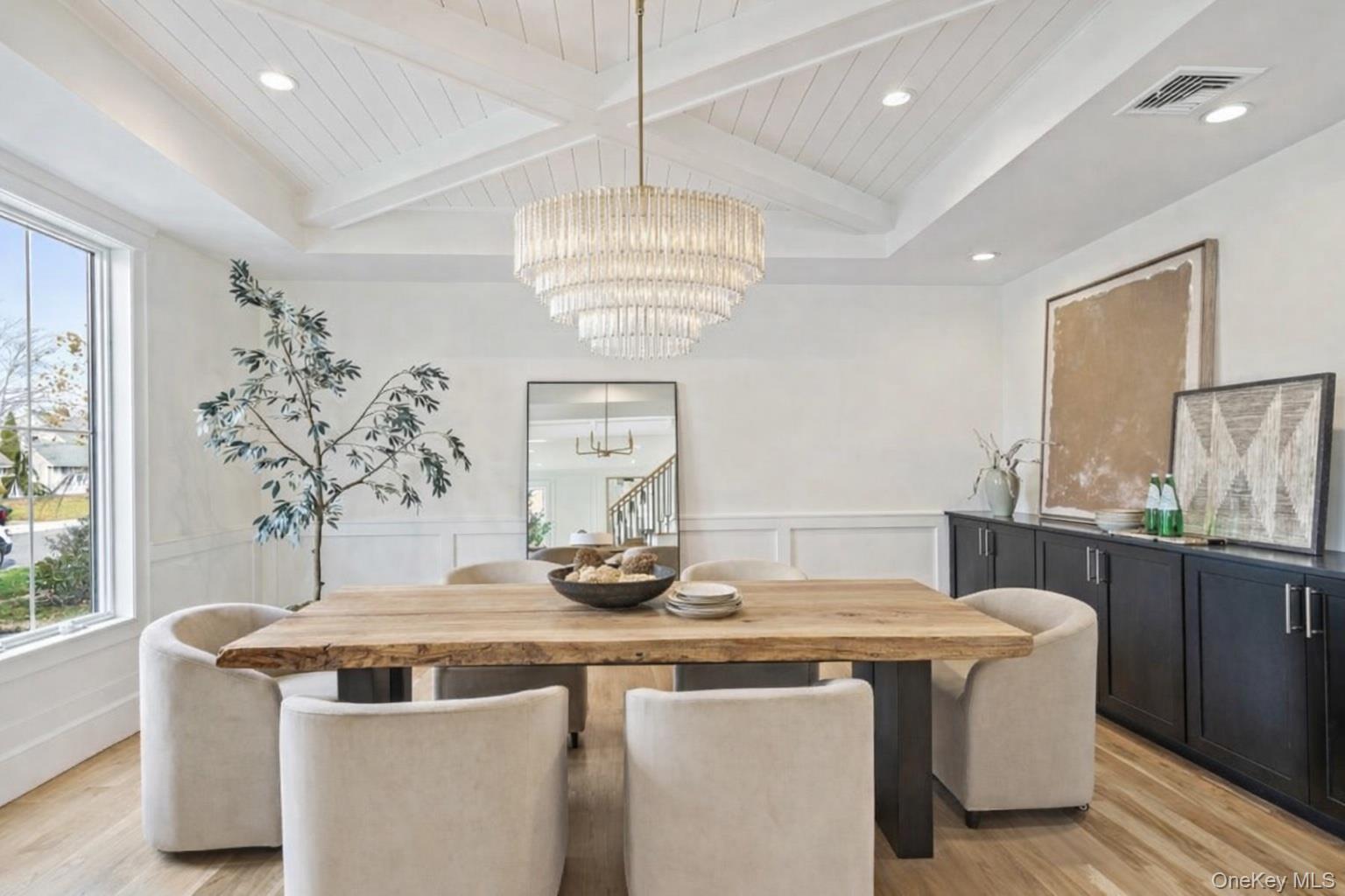 Dining space with wainscoting, a wooden ceiling with exposed beams, a decorative wall, plenty of natural light, and light wood finished floors