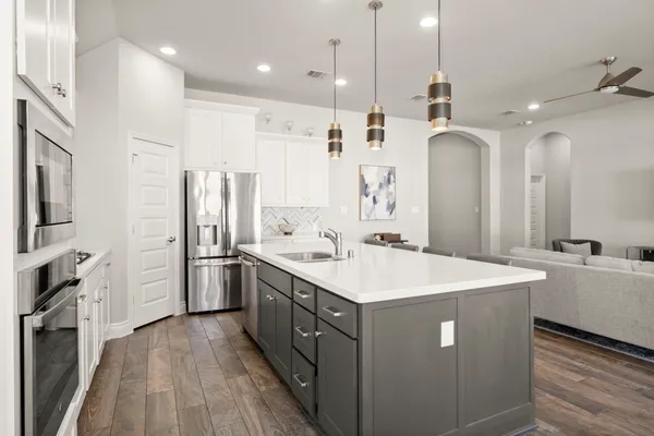 a large kitchen with stainless steel appliances a refrigerator a sink dishwasher a kitchen island with wooden floor and cabinets