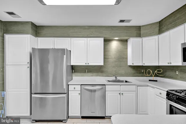 a kitchen with stainless steel appliances a refrigerator a sink and white cabinets