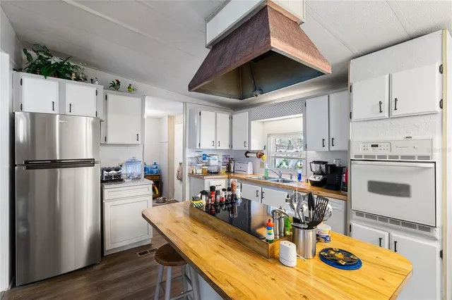 a kitchen with stainless steel appliances granite countertop a refrigerator a stove top oven a sink dishwasher and white cabinets with wooden floor