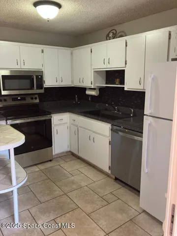 a white kitchen with granite countertop a stove a sink and white cabinets