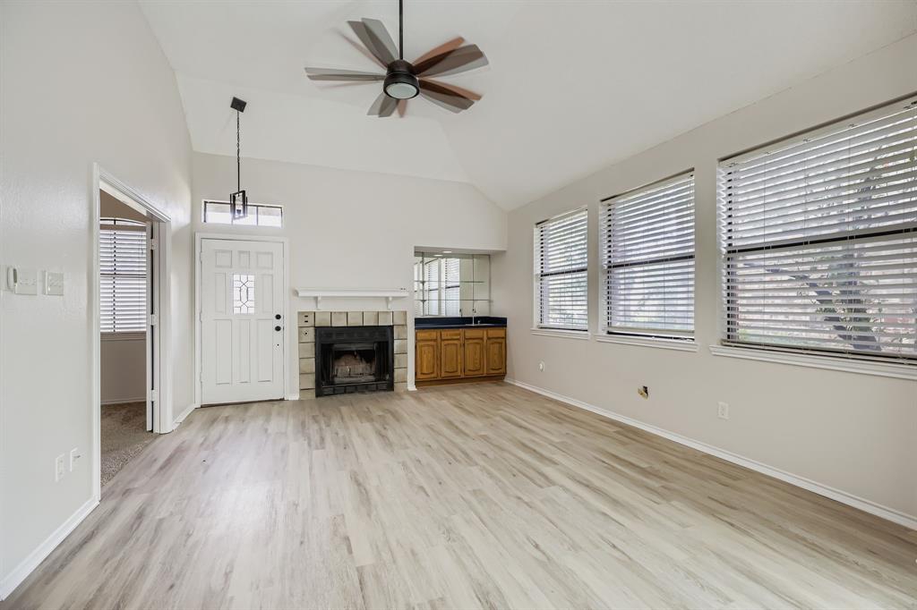 4319 Harvest Hill Road Carrollton, TX 75010 - Photo 7 of 28 Unfurnished living room featuring light wood-type flooring, a ceiling fan, a tiled fireplace, and high vaulted ceiling