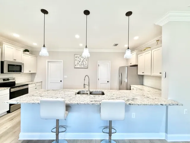 a kitchen with kitchen island stainless steel appliances a sink center island a stove white cabinets and chairs