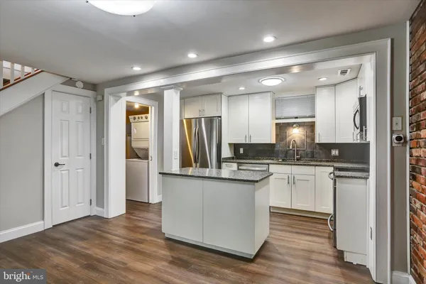 a kitchen with stainless steel appliances granite countertop a refrigerator a sink dishwasher a stove and a dining table with wooden floor