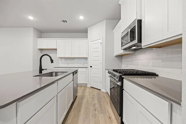 a large kitchen with stainless steel appliances a white stove top oven a sink and dishwasher with wooden floor