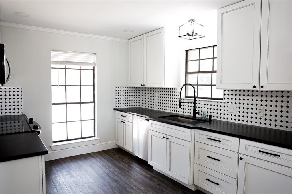 10575 Friendship Road Pilot Point, TX 76258 - Photo 24 of 32 Modern kitchen featuring white cabinetry with dark hardware, black countertops, and a distinctive black and white tiled backsplash