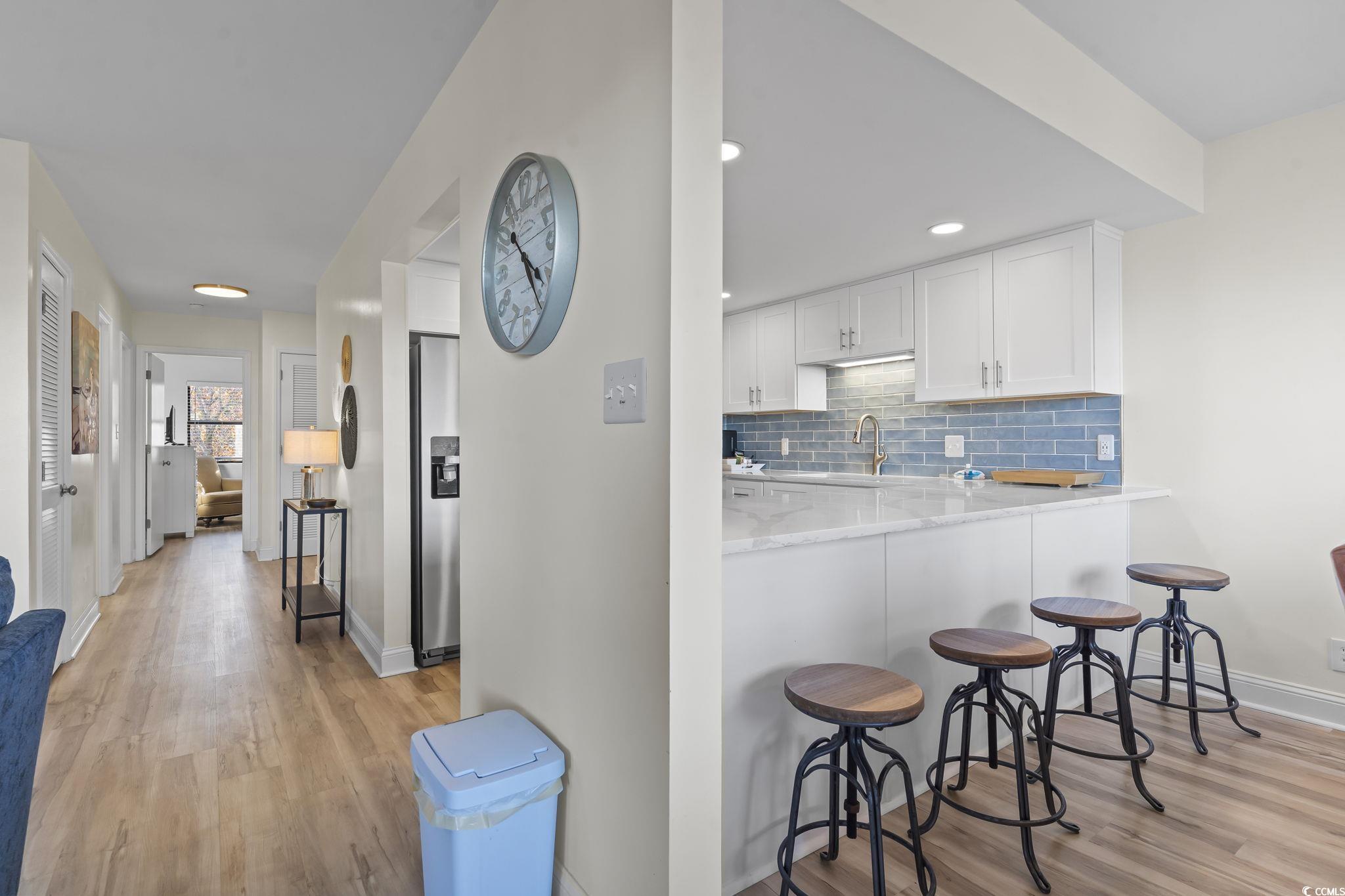 310 3rd Avenue North, Unit A2 Surfside Beach, SC 29575 - Photo 10 of 40 Kitchen featuring white cabinetry, tasteful backsplash, light stone counters, light wood-type flooring, and a kitchen breakfast bar