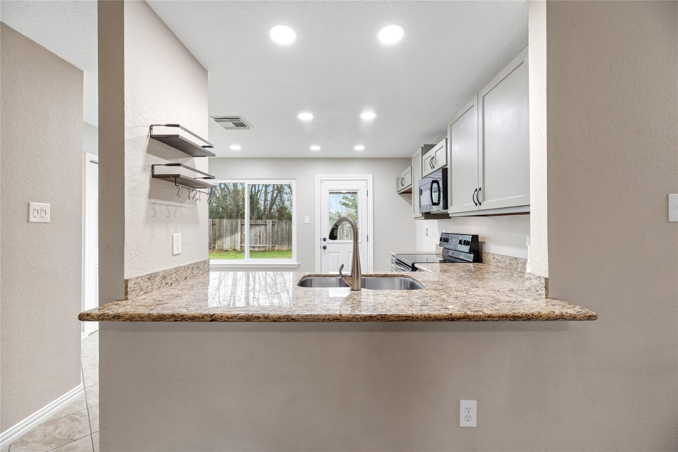 24006 Lazy Kay Lane Hockley, TX 77447 - Photo 6 of 21 Modern kitchen with granite countertops and ample cabinet space. It features an open layout with a view of the backyard and natural reserve behind the home through the windows.