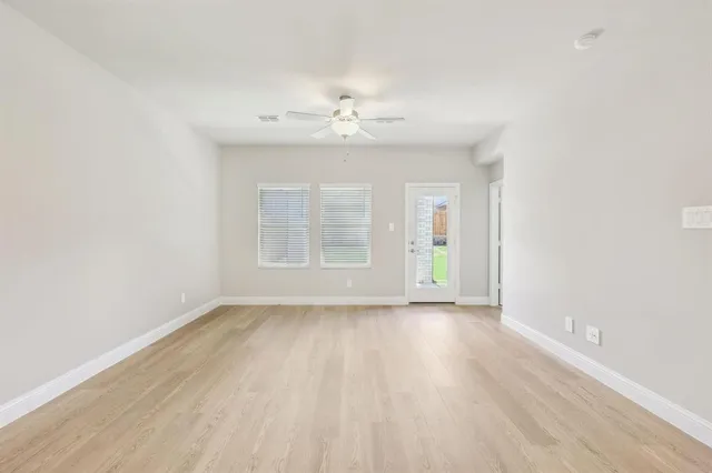 an empty room with wooden floor chandelier fan and windows