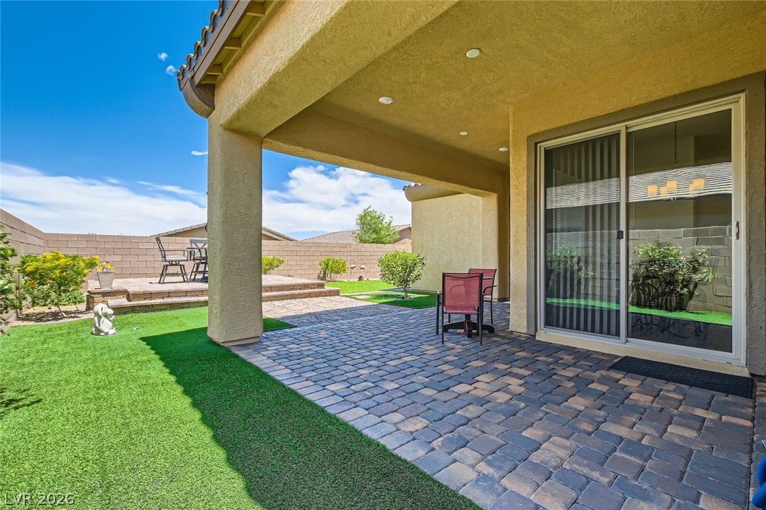 498 Pebble Run Avenue Henderson, NV 89011 - Photo 21 of 47 An inviting covered patio featuring paver stones leads to a manicured yard with a raised seating area.
